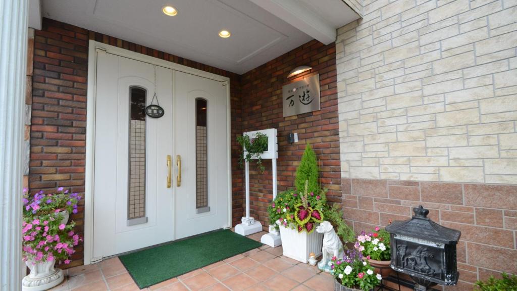 una casa de ladrillo con una puerta blanca y algunas flores en Shikisai no Sato Manyu en Kirishima