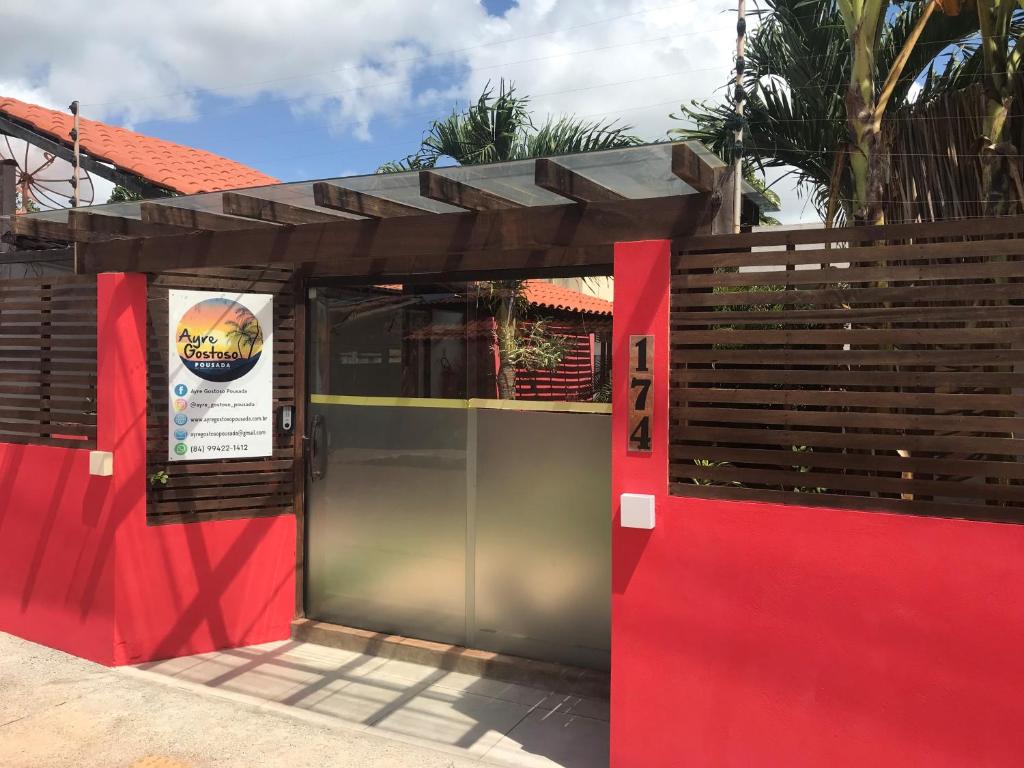 - un bâtiment avec une porte rouge et un panneau. dans l'établissement AYRE GOSTOSO POUSADA, à São Miguel do Gostoso