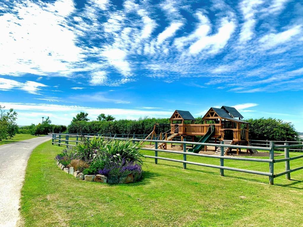 a log house with a playground and a fence at Pentire Coastal Holiday Park in Bude