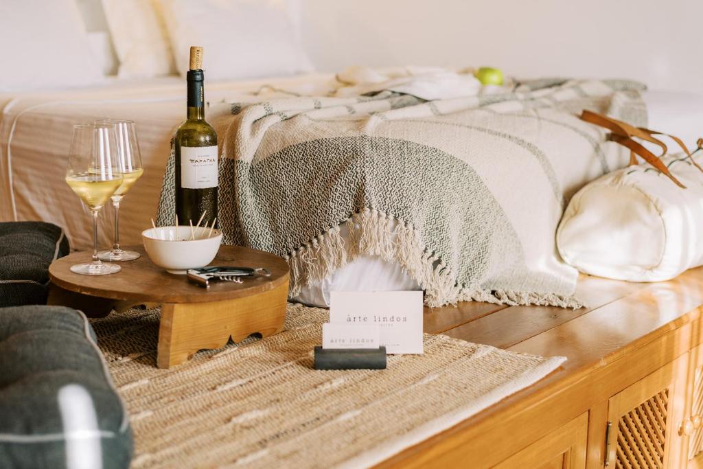 ARTE LINDOS SUITES في ليندوس: سرير مع زجاجة من النبيذ وكأس