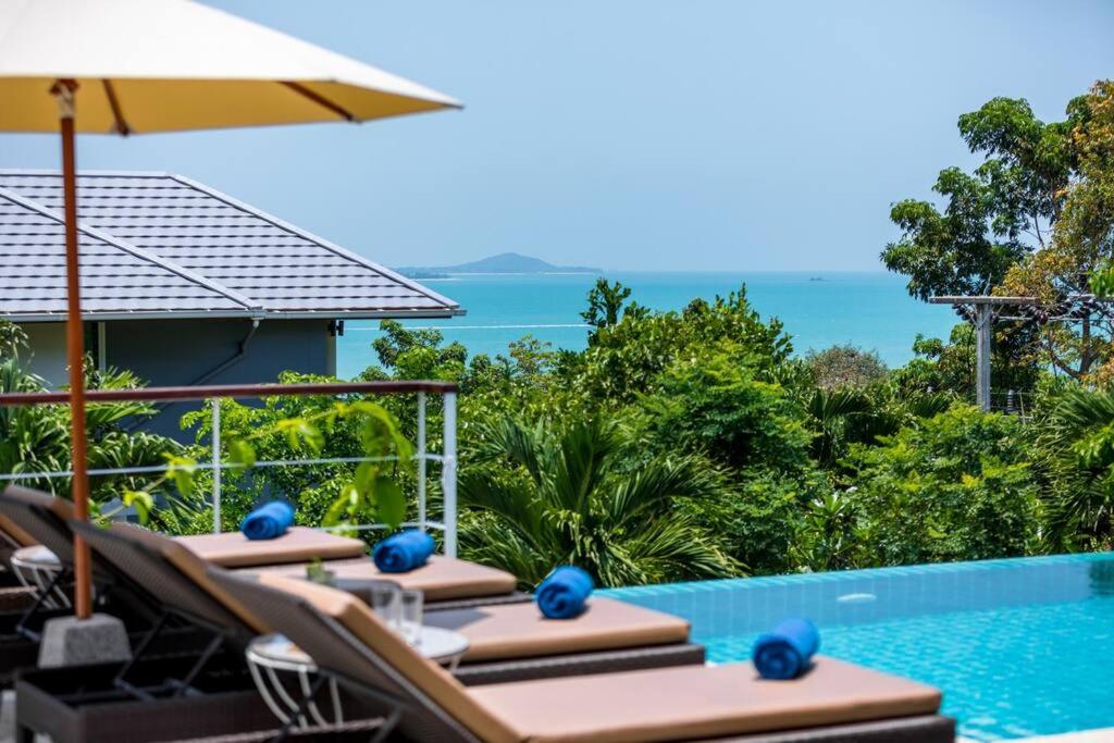 een zwembad met stoelen en een parasol en de oceaan bij Villa Wassana - Sunset View 5Bed in Koh Samui 