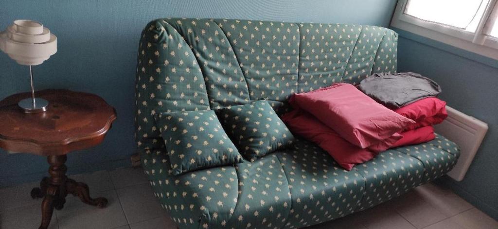 un sofá verde con almohadas junto a una mesa en Studio au calme en Péronnas