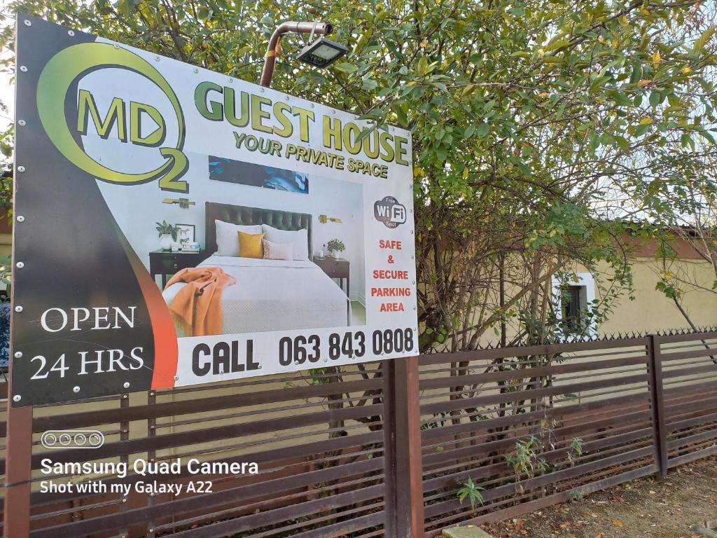 un cartel de la casa de huéspedes frente a una valla con cama en MD VIP Guesthouse - Debruin Ermelo, en Ermelo