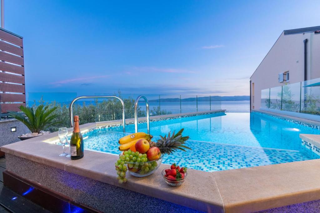 a table with fruit and a bottle of wine next to a swimming pool at Apartments Villa Tomaš in Brela