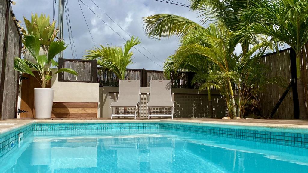 a swimming pool with two lawn chairs and trees at Tala Lodge Bonaire in Kralendijk