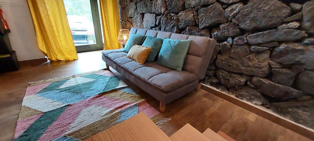 a couch in a living room with a stone wall at Ti Chôa - Casa da Praça in Angra do Heroísmo