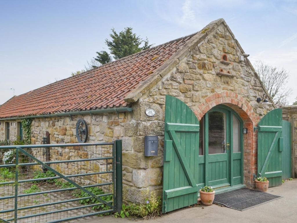 um pequeno edifício de pedra com portas verdes e um portão em The Workshop em Newton on the Moor