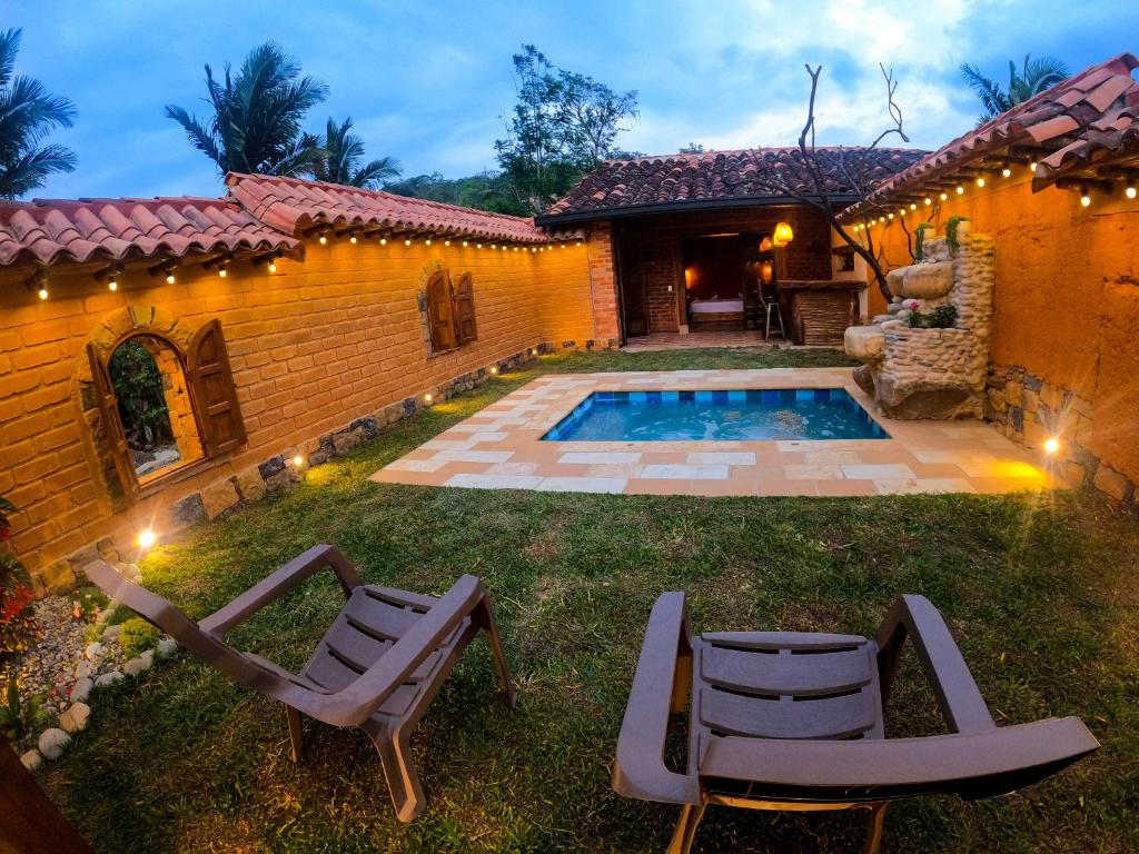 un patio trasero con piscina, 2 sillas y una casa en Cabañas el Nopal, en San Gil