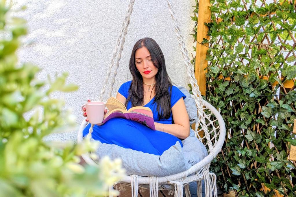 a woman sitting in a hammock reading a book and drinking coffee at Queen Apartment in Uelzen