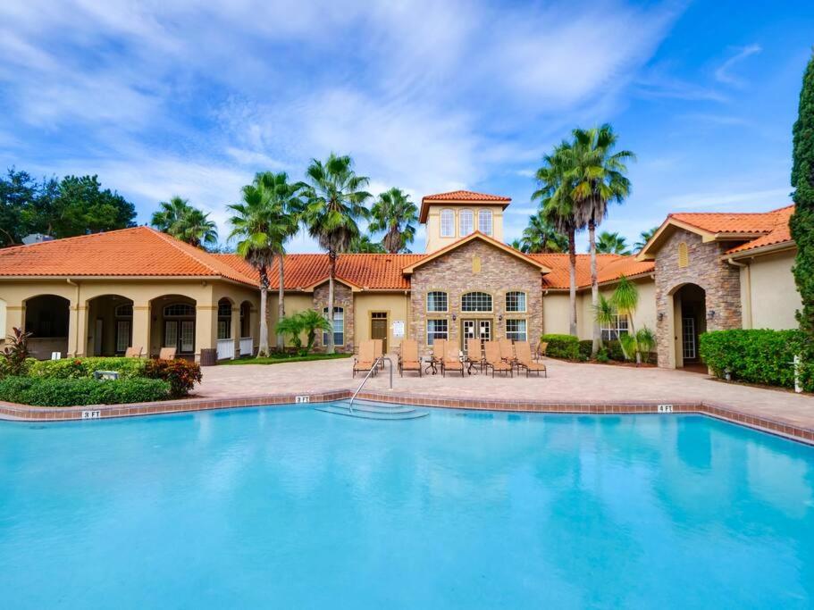 a large swimming pool in front of a house with palm trees at Florida Vacation Condo - No Resort Fees in Kissimmee