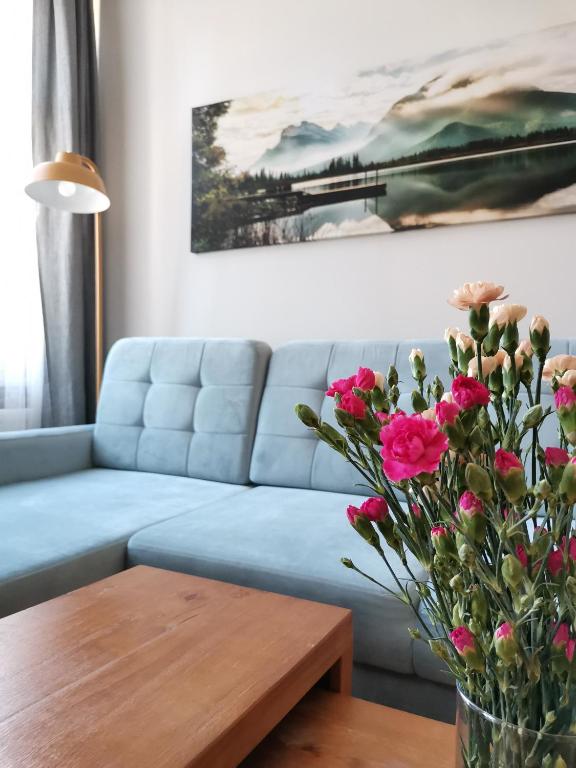 a living room with a blue couch and a table with flowers at Apartamenty w ścisłym centrum Kupiecka-Drzewna in Zielona Góra