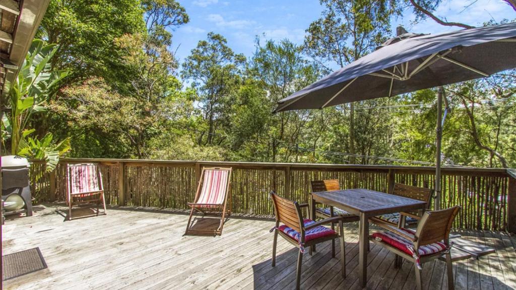 a table and chairs on a deck with an umbrella at Tea Tree House - Pearl Beach in Pearl Beach