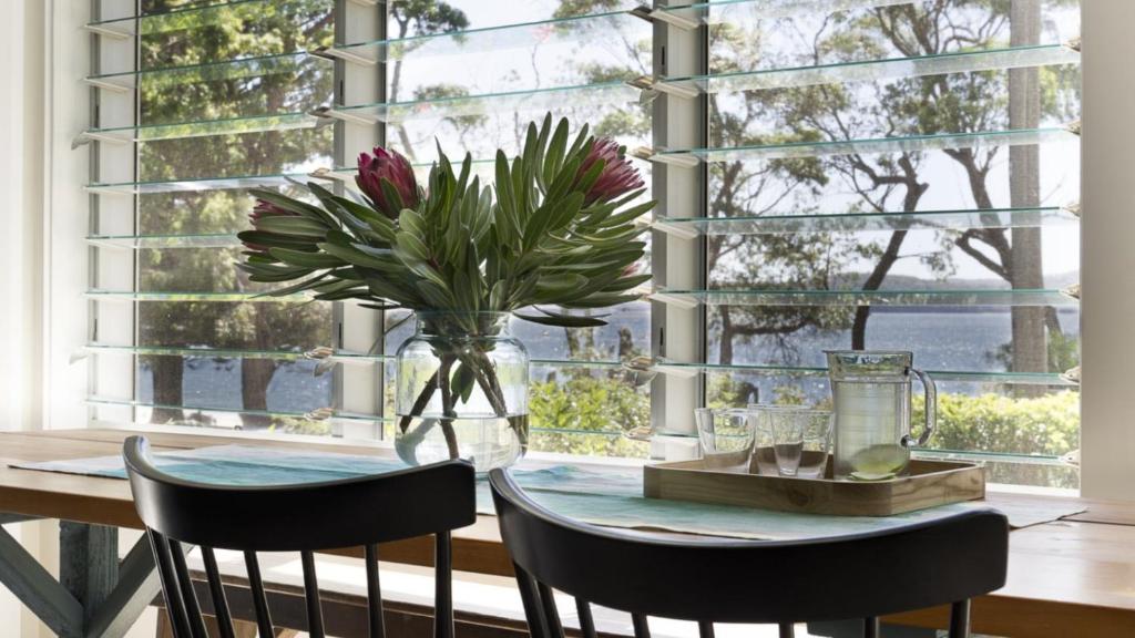 a dining room table with a vase of flowers on it at Beach Vista - A Designer Delight Oposite The Beach in Pearl Beach