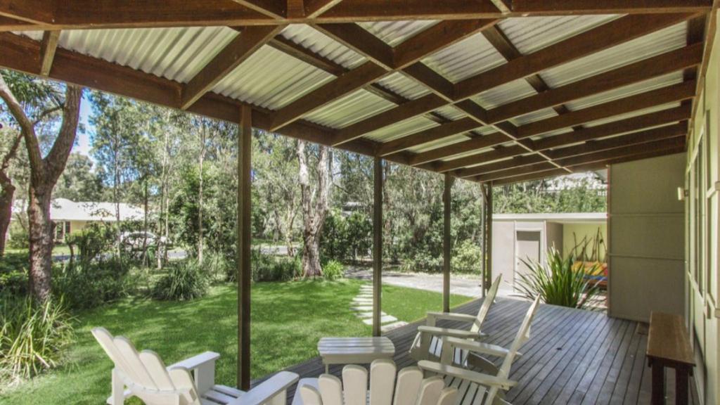 a patio with white chairs on a wooden deck at Coastal Chic Holiday Cottage in Pearl Beach