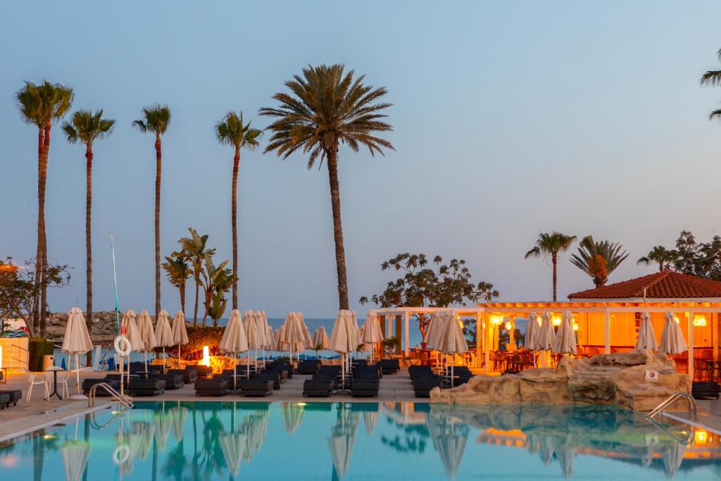 a swimming pool with umbrellas and chairs and palm trees at Pavlo Napa Beach Hotel in Ayia Napa