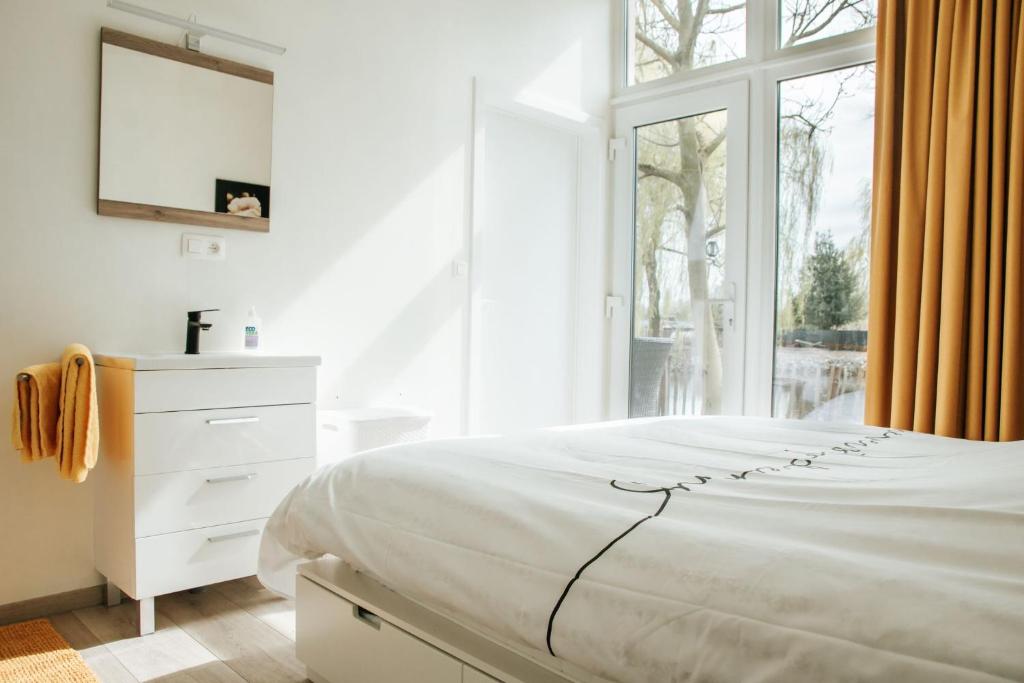 a white bedroom with a bed and a window at Trendy chalet aan visvijver in Hamme