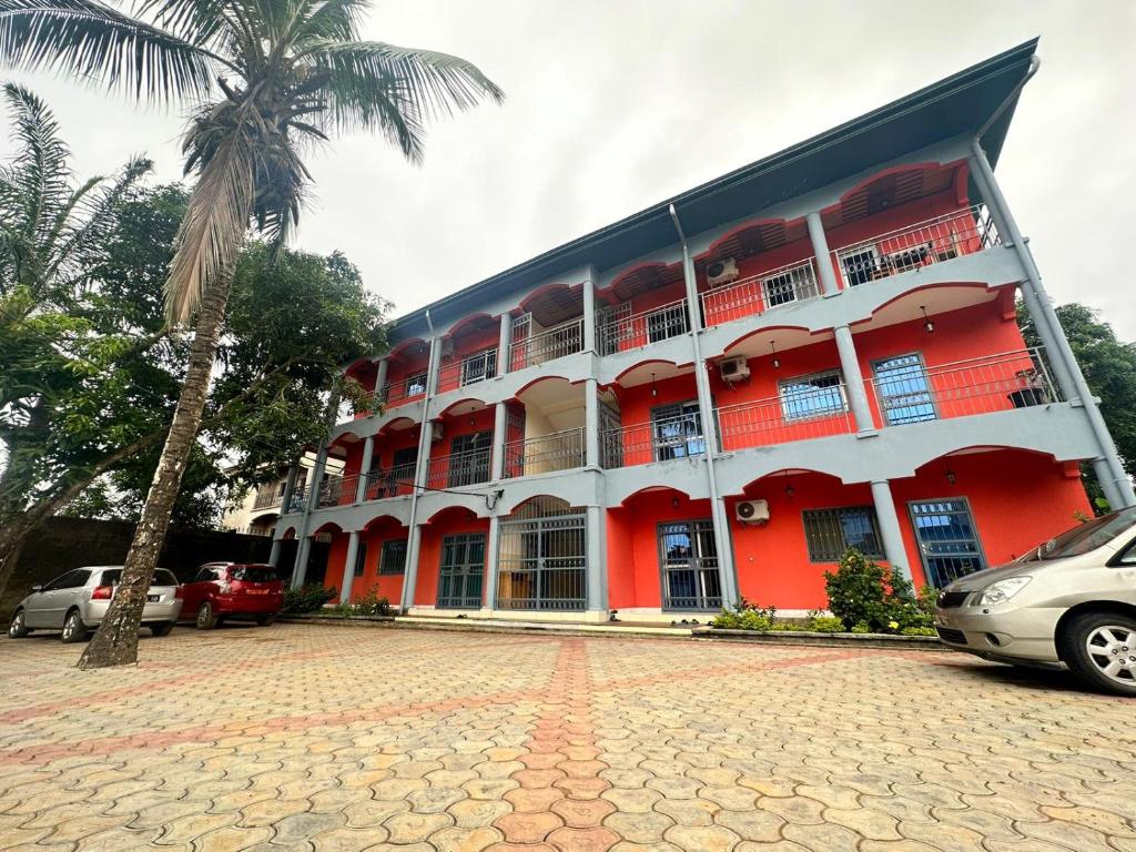 un edificio rojo con una palmera delante en appartements meublés à Logbessou, en Douala