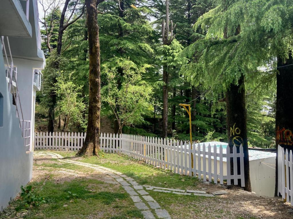 una cerca blanca frente a una casa con un árbol en Himtrek Stays,Mcleodganj en McLeod Ganj