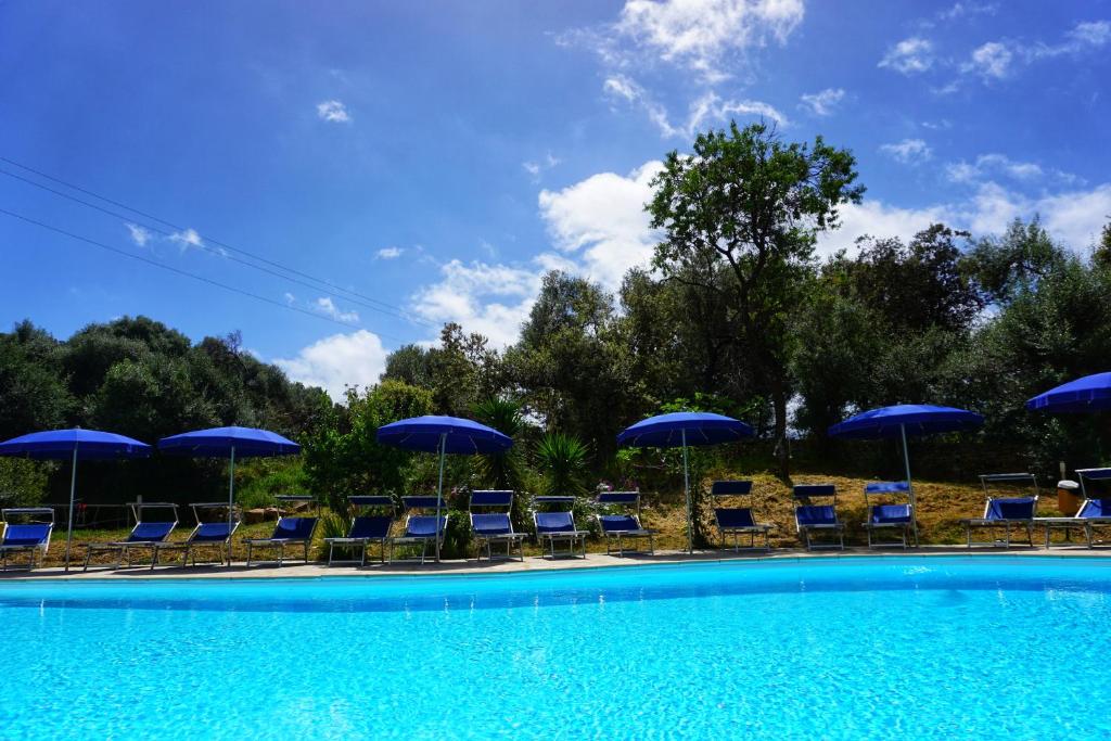 a swimming pool with blue chairs and umbrellas at Résidence Itylon in Cargèse
