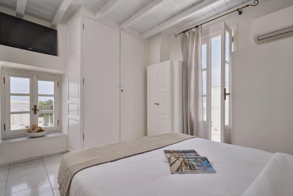 a white bedroom with a bed with a book on it at Myconian Princess in Mikonos