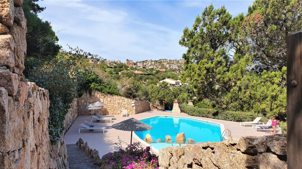 a pool with chairs and an umbrella next to a stone wall at Monica Luxury House in Porto Cervo
