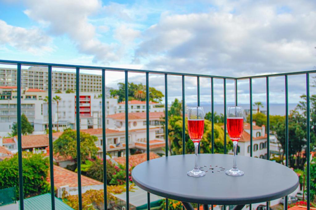 Dois copos de vinho tinto numa mesa na varanda. em Casal da Penha Apartments no Funchal