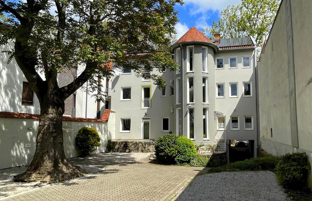 ein großes weißes Gebäude mit einem Baum davor in der Unterkunft Benevia Apartments in Pécs