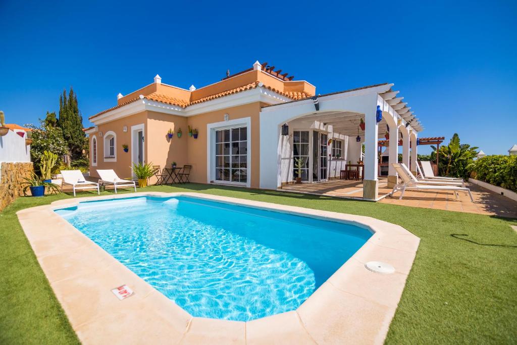 a villa with a swimming pool in front of a house at El Olivar Beach Golf in Caleta De Fuste