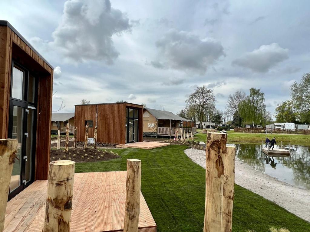 a house with wooden posts in front of a pond at Tiny House in Kesteren