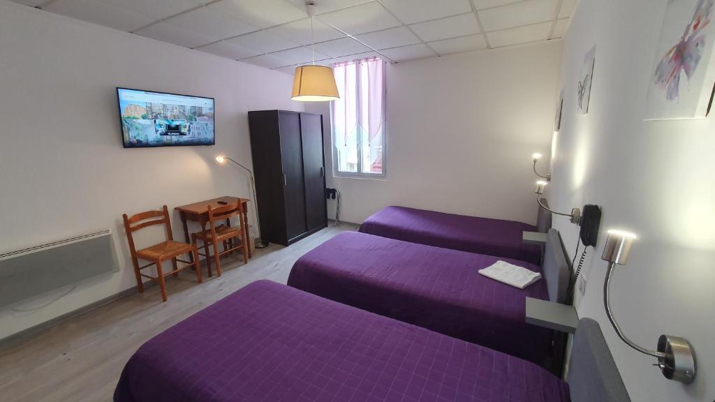 une chambre d'hôtel avec des lits violets et une table dans l'établissement Hôtel du Roc, à Castellane