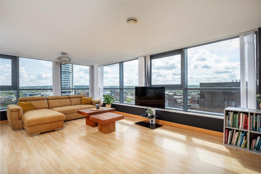 uma sala de estar com um sofá e uma televisão e janelas em Leeds Most Stunning Penthouse! - Sleeps 8 em Leeds