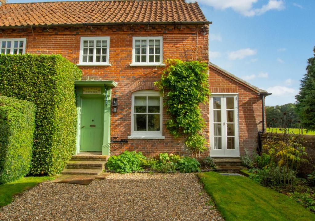 a brick house with a green door and ivy at Baytree Cottage in Melton Constable