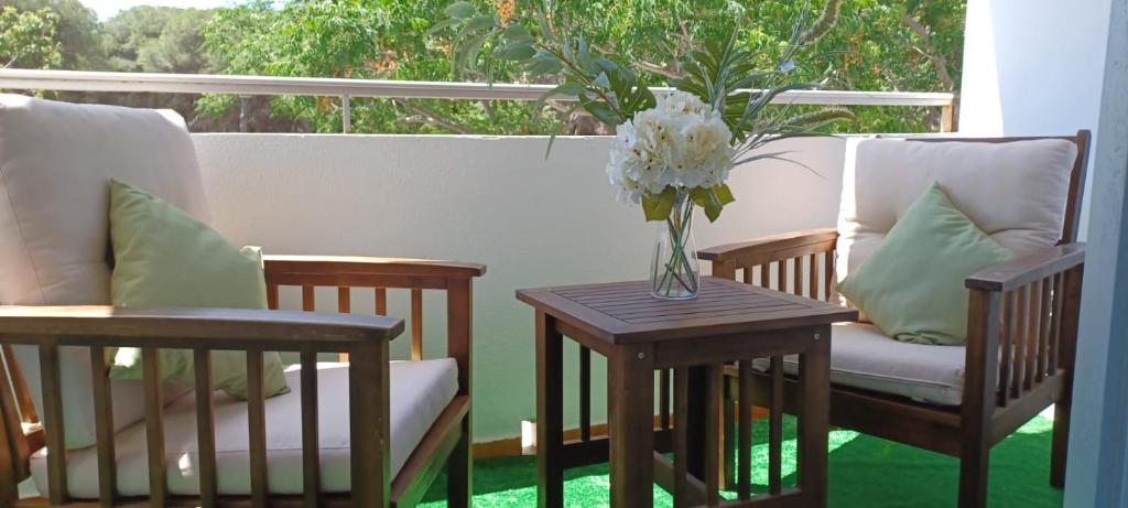 dwa krzesła i stół z wazonem kwiatów na ganku w obiekcie Las Dunas w mieście El Puerto de Santa María