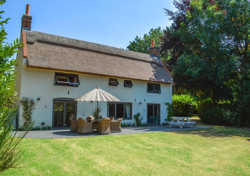 a large white house with chairs and an umbrella at Keepers Cottage in Panxworth