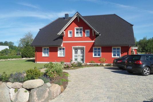a red house with a car parked in a driveway at Am Park, App Dünennest in Wustrow