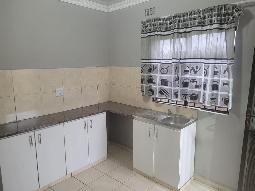 a kitchen with white cabinets and a sink and a window at Mavundla lifestyle lodge in Empangeni
