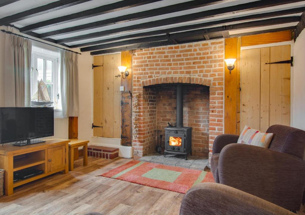 a living room with a brick fireplace and a television at Reading Room Cottage in Overstrand