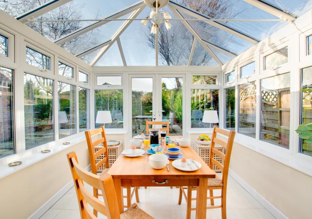 a conservatory with a wooden table and chairs at Sunset Cottage in Hickling