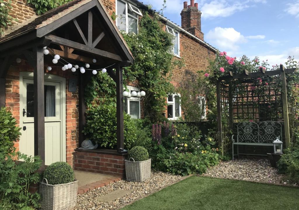 a garden with a gate and a bench in front of a house at Thimble Cottage in Dersingham