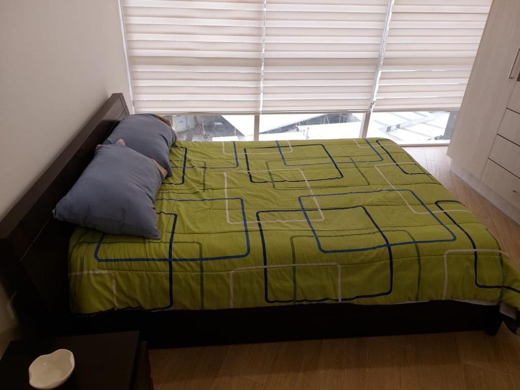 ein Bett mit einer grünen Decke und einem Fenster in der Unterkunft Departamento confortable en Quito in Quito