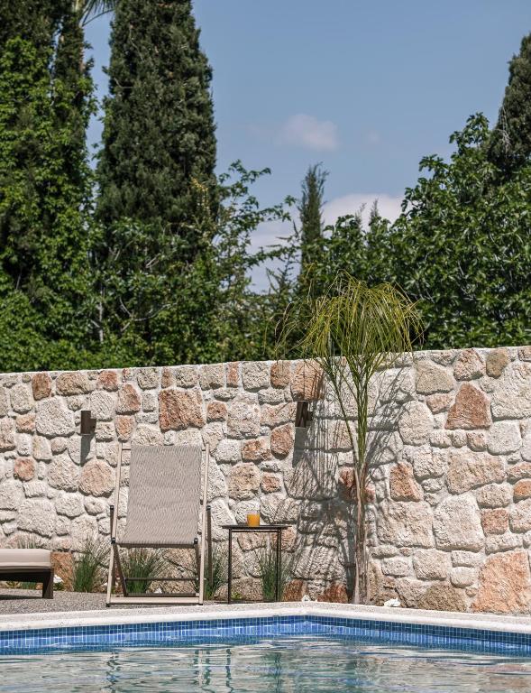 a chair next to a stone wall next to a swimming pool at VagAthan - Lux Holidays in Afitos