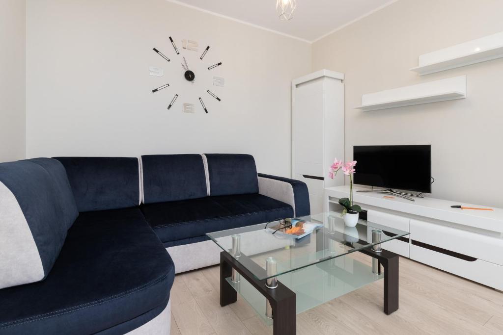 a living room with a blue couch and a clock on the wall at Gdańsk Aleja Jana Pawła II Apartment with Parking and Balcony by Renters in Gdańsk