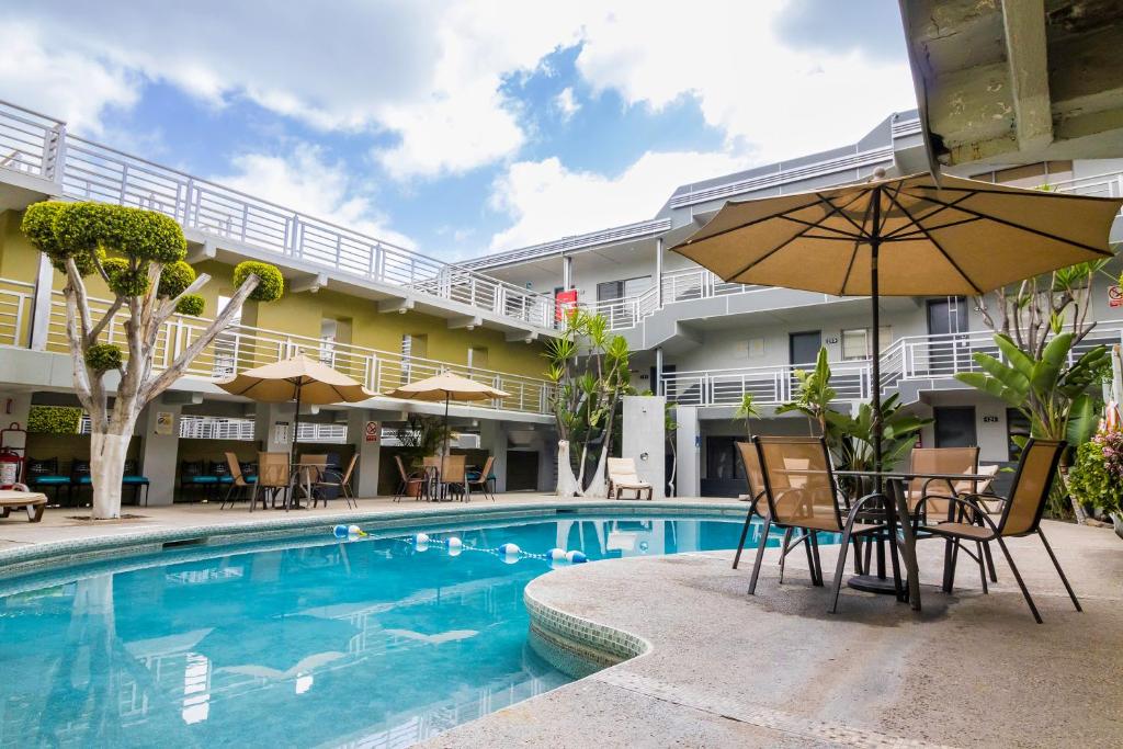 ein Hotelpool mit Stühlen und einem Sonnenschirm in der Unterkunft Baja Inn Hoteles La Mesa in Tijuana