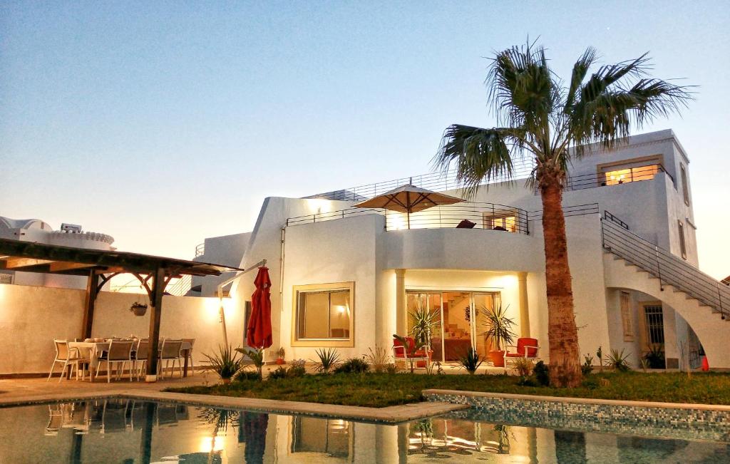 a house with a palm tree in front of a swimming pool at Villa Kenais Sunset in Taguermess