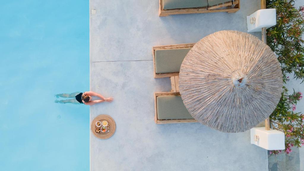 Ein Mann steht neben einem Pool mit einem großen Regenschirm. in der Unterkunft Irida Vacation suites in Kastraki Naxos