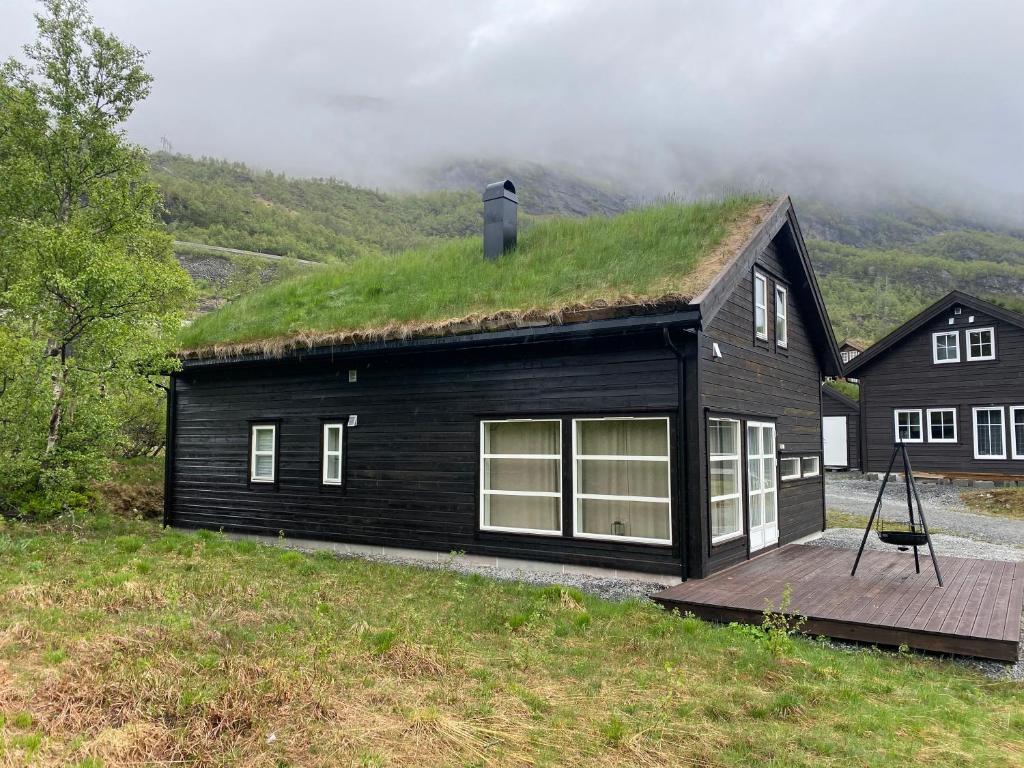 una casa negra con techo de hierba y terraza de madera en Hytte på fjellet, en Håra