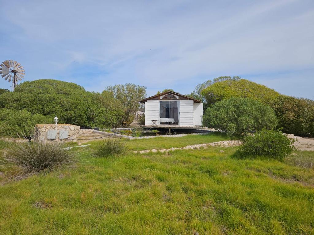 una pequeña casa blanca en un campo con un molino de viento en Aintree Lodge - Yoga Den en Langebaan