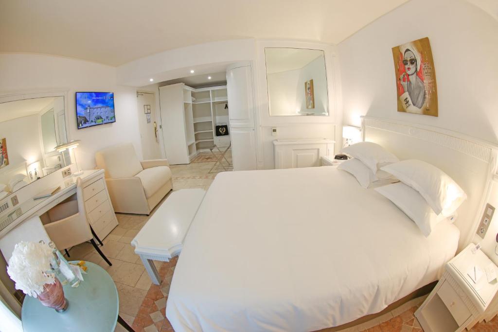 a white bedroom with a large bed and a desk at Hôtel L'Abbaye in Calvi