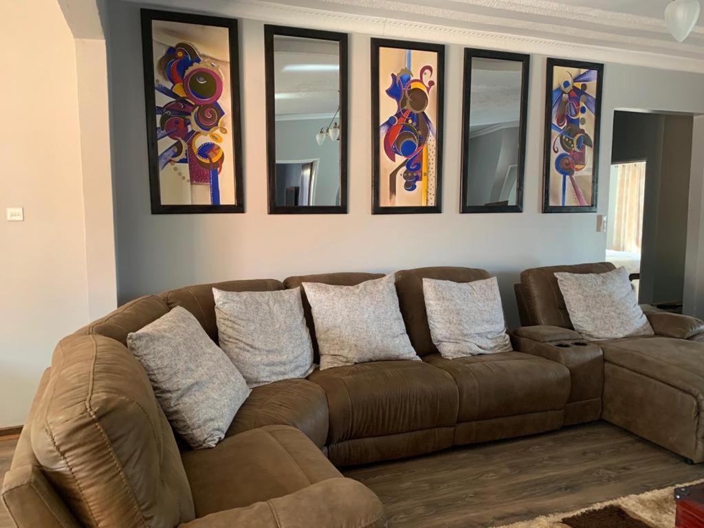 um sofá castanho numa sala de estar com pinturas na parede em Beautiful guesthouse with pool and solar - 2057 em Victoria Falls