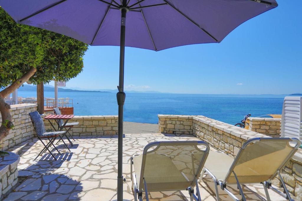 un paraguas púrpura y sillas en un patio con vistas al océano en Kaminaki Beachfront Apartments, en Nisakion